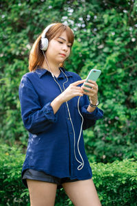 Young woman using mobile phone while standing in park