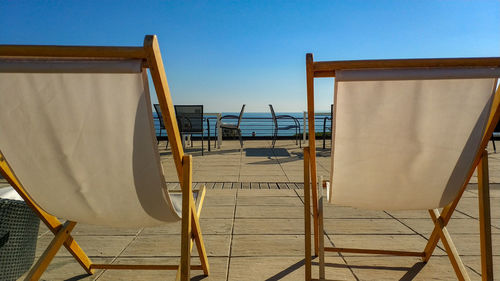 Empty chairs by sea against clear blue sky