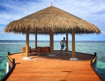 Rear view of man standing in gazebo over sea against sky