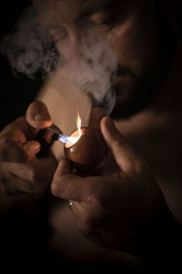 Close-up of man lighting smoking pipe in darkroom