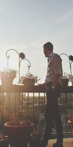 Side view of man standing by railing against sky in city