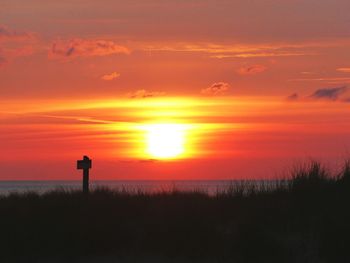 Silhouette man standing by sea against orange sky