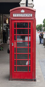 Red telephone booth on sidewalk in city