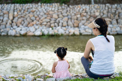 Adorable girl sitting at pond with her mother in summer.