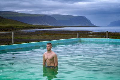 Portrait of shirtless man in swimming pool against sky