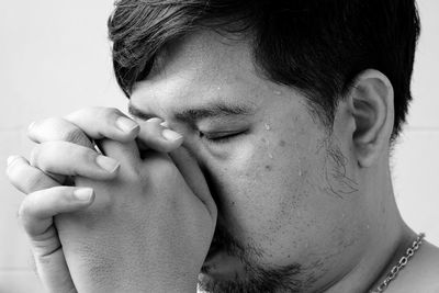 Close-up of man with eyes closed and hands clasped praying against gray background