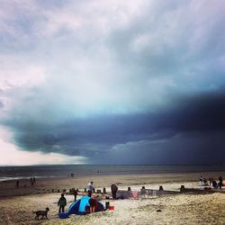 People on beach against cloudy sky