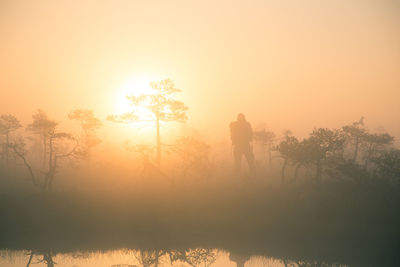 Silhouette man standing on field against orange sky during sunrise