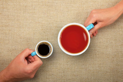 Cropped hands of people with coffee and tea in cups on table