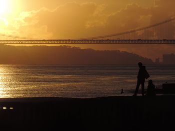 Silhouette friends against april 25th bridge over river during sunset