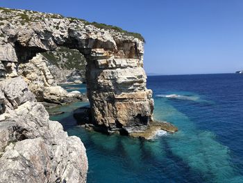 Rock formations by sea against clear blue sky