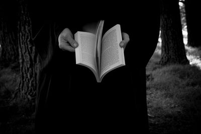 Midsection of person holding book in forest