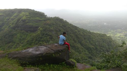 Man sitting on rock while looking at green landscape