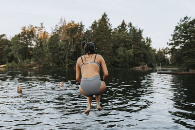 Rear view of woman standing by lake against sky