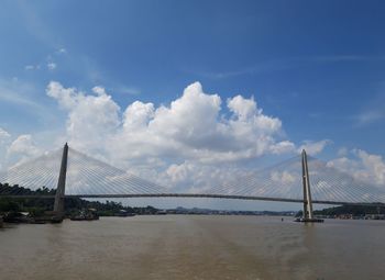 Suspension bridge over river against cloudy sky