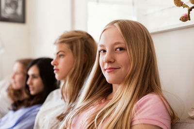 Portrait of confident teenage girl sitting on sofa while friends watching tv at home