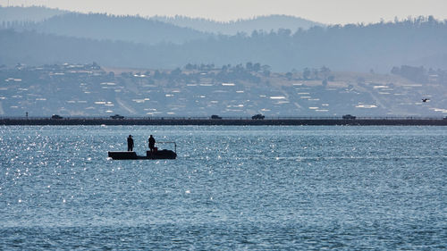 Silhouette men on boat in lake against mountains