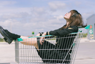 Young woman sitting in shopping cart during sunny day