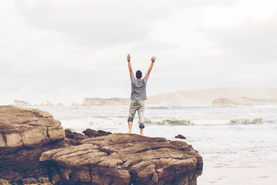 Rear view of man standing on rock by sea against sky