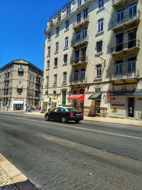 Cars on road by buildings against sky in city