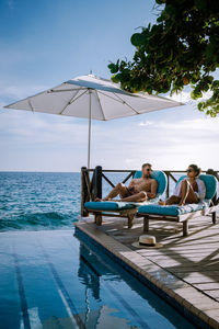 People sitting by swimming pool against sky