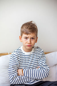 Portrait of boy sitting on bed at home