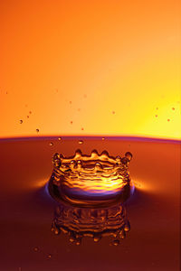 Close-up of drop splashing on water against orange background