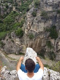 Rear view of man sitting at cliff against rocky formation