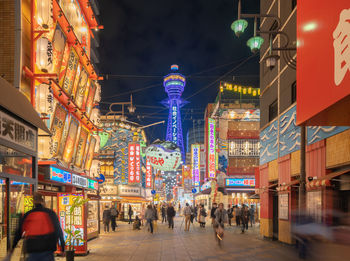 People walking on illuminated street amidst buildings at night