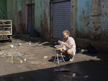 Full length of woman sitting on sidewalk against building