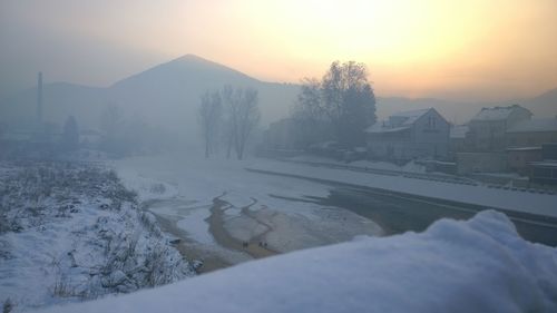 Snow covered landscape against sky during sunset