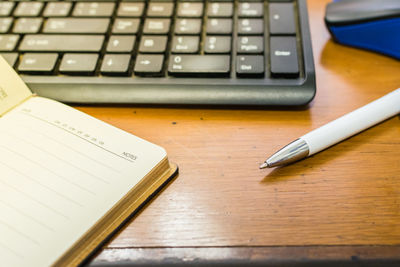 Close-up of computer keyboard with pen and book on table