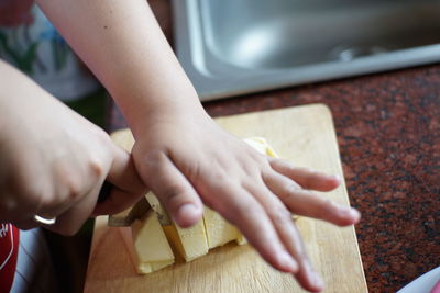 Cropped hands of person cutting food on board in kitchen
