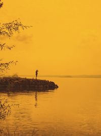 Silhouette person standing by sea against sky during sunset