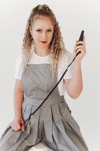 Portrait of young woman using mobile phone while standing against white background