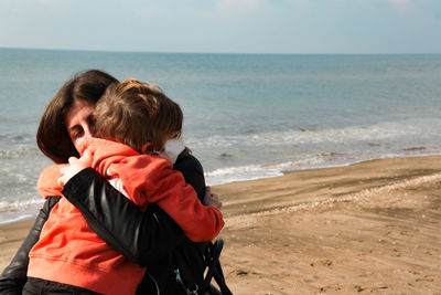 Rear view of mother and daughter on beach against sky