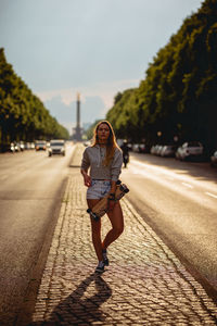Full length portrait of woman with skateboard standing on roadside