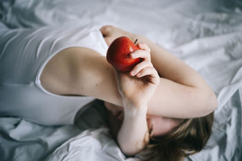 High angle view of woman with apple lying on bed at home