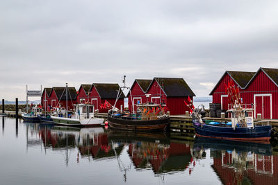 Boats moored in harbor by buildings against sky