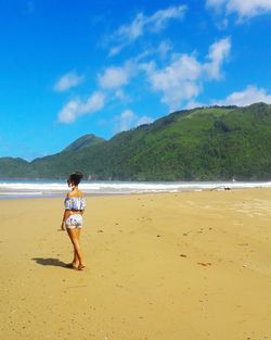 Woman walking at beach against mountains in sunny day