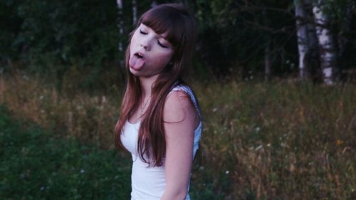 Woman standing with tongue out against trees in forest