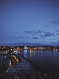 Illuminated city by sea against sky at dusk