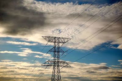 Low angle view of electricity pylon against cloudy sky