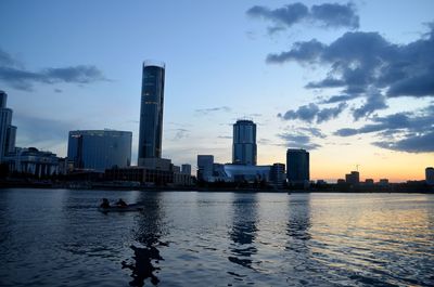 River by modern buildings against sky during sunset