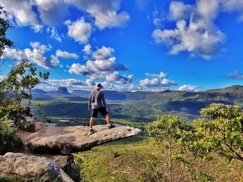 Rear view of man standing on cliff against blue sky