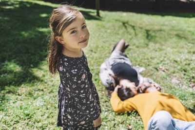 Portrait of cute daughter standing against parents lying on grassy field in park