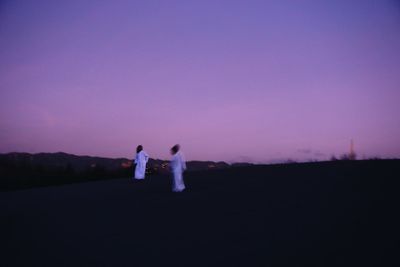 Couple standing on field against sky at dusk