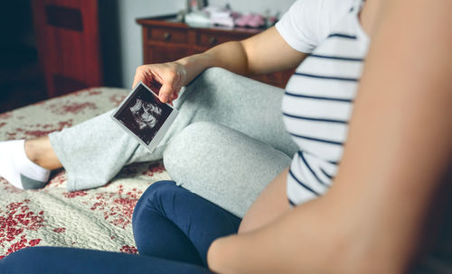 Midsection of couple holding ultrasound scan at bed