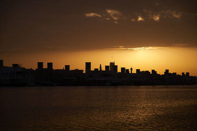 Silhouette buildings by sea against sky during sunset