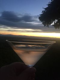 Close-up of hand holding drink against sunset sky
